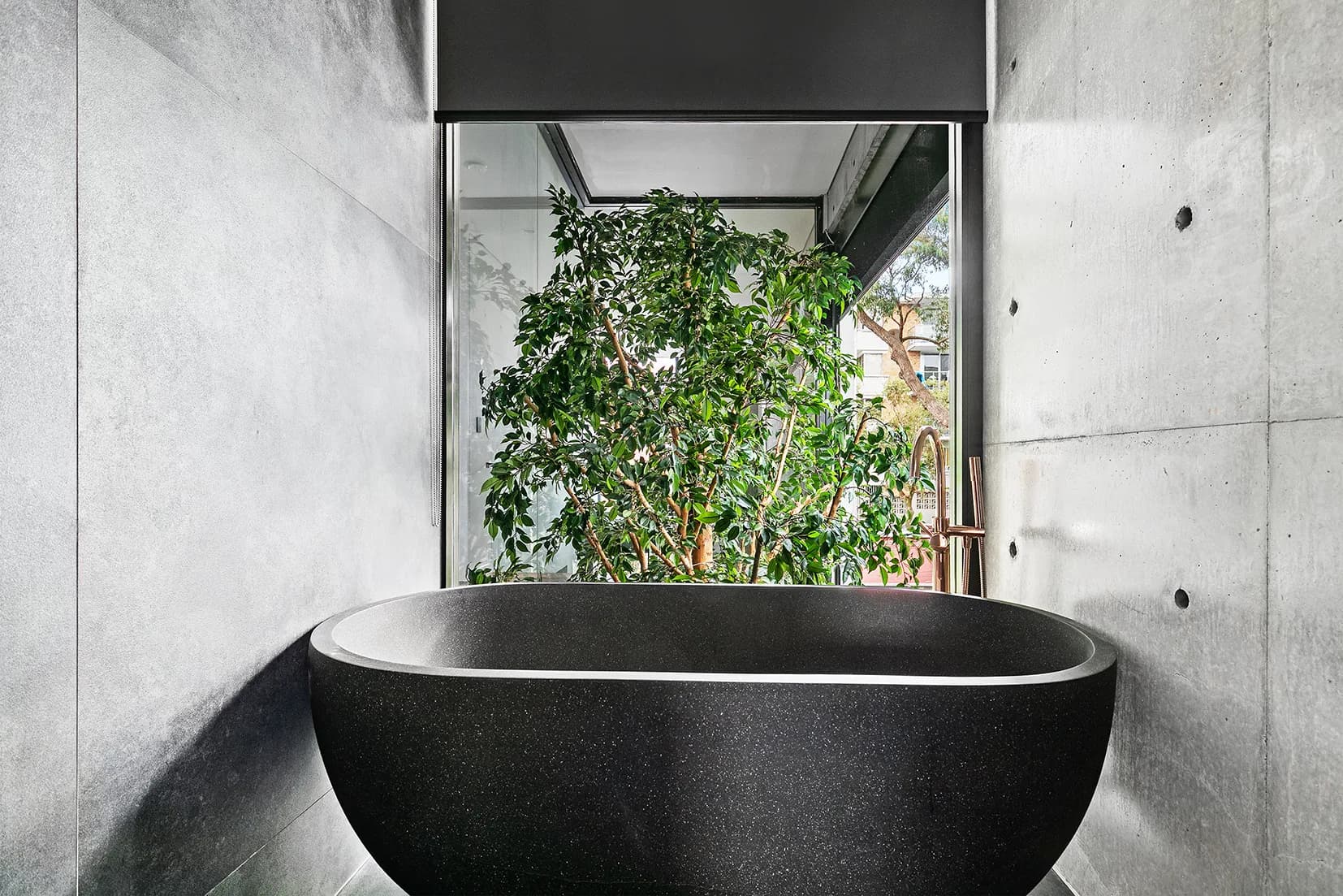 Natural stone freestanding bath at The Arc beneath the garden atrium's greenery