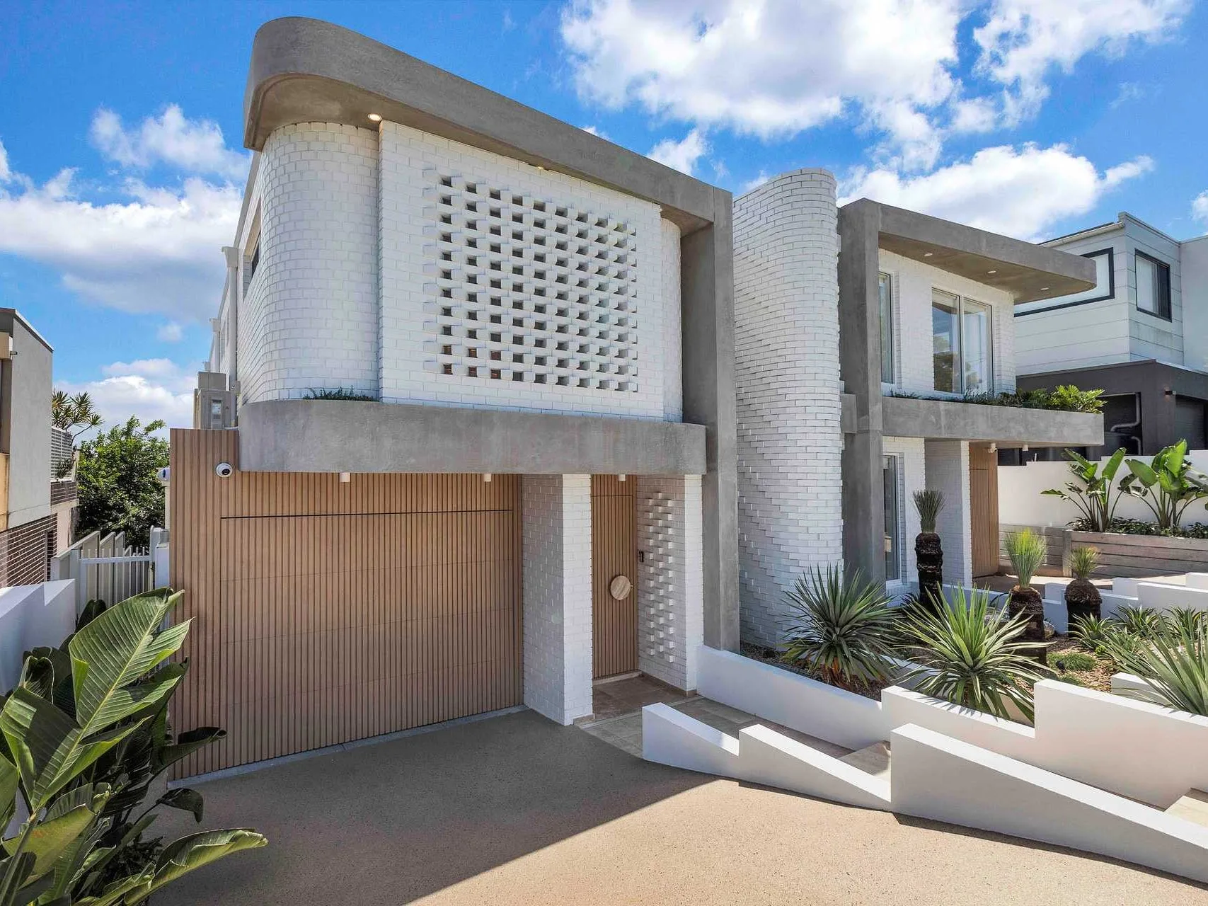 Street elevation of Hillary, a completed white-brick duplex in Matraville with a curved breeze-block screen and battened timber garage door